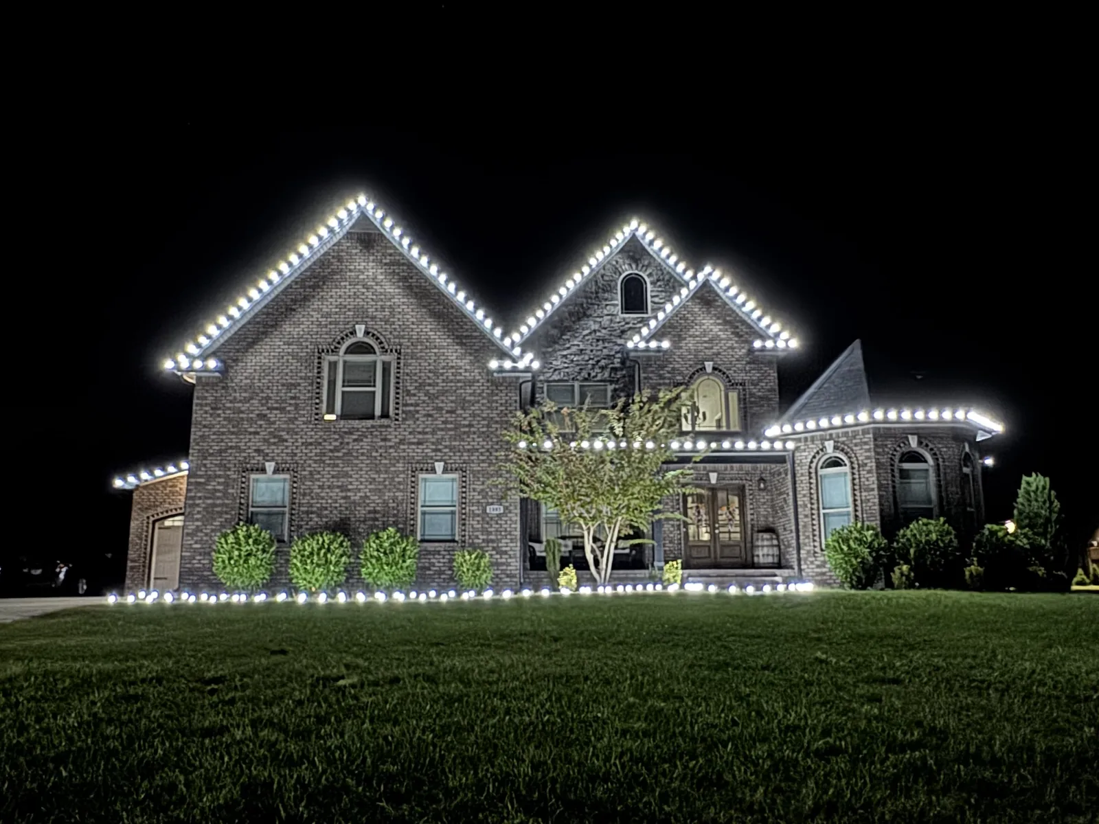 Cool white Christmas lights outlining the roof peaks and shrubs of a brick home